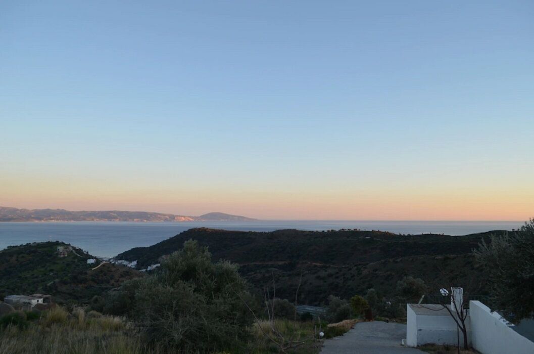 A coastal landscape with a clear sky, a distant view of the sea, and a hilly terrain.