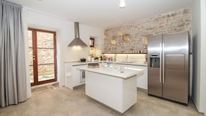 Una cocina moderna con una isla central, una pared de piedra y un refrigerador grande.