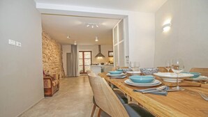 Un comedor con una mesa de madera dispuesta para cuatro personas, una pared de piedra y una cocina al fondo.