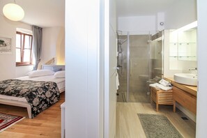 Une chambre à coucher avec un lit, une table de chevet et une fenêtre avec des rideaux. La pièce est dotée d’un plancher en bois et d’un tapis rouge.