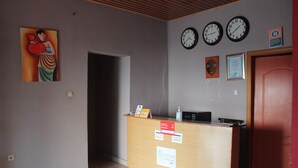 A reception area with a wooden desk, three wall clocks, a framed certificate, and a painting.