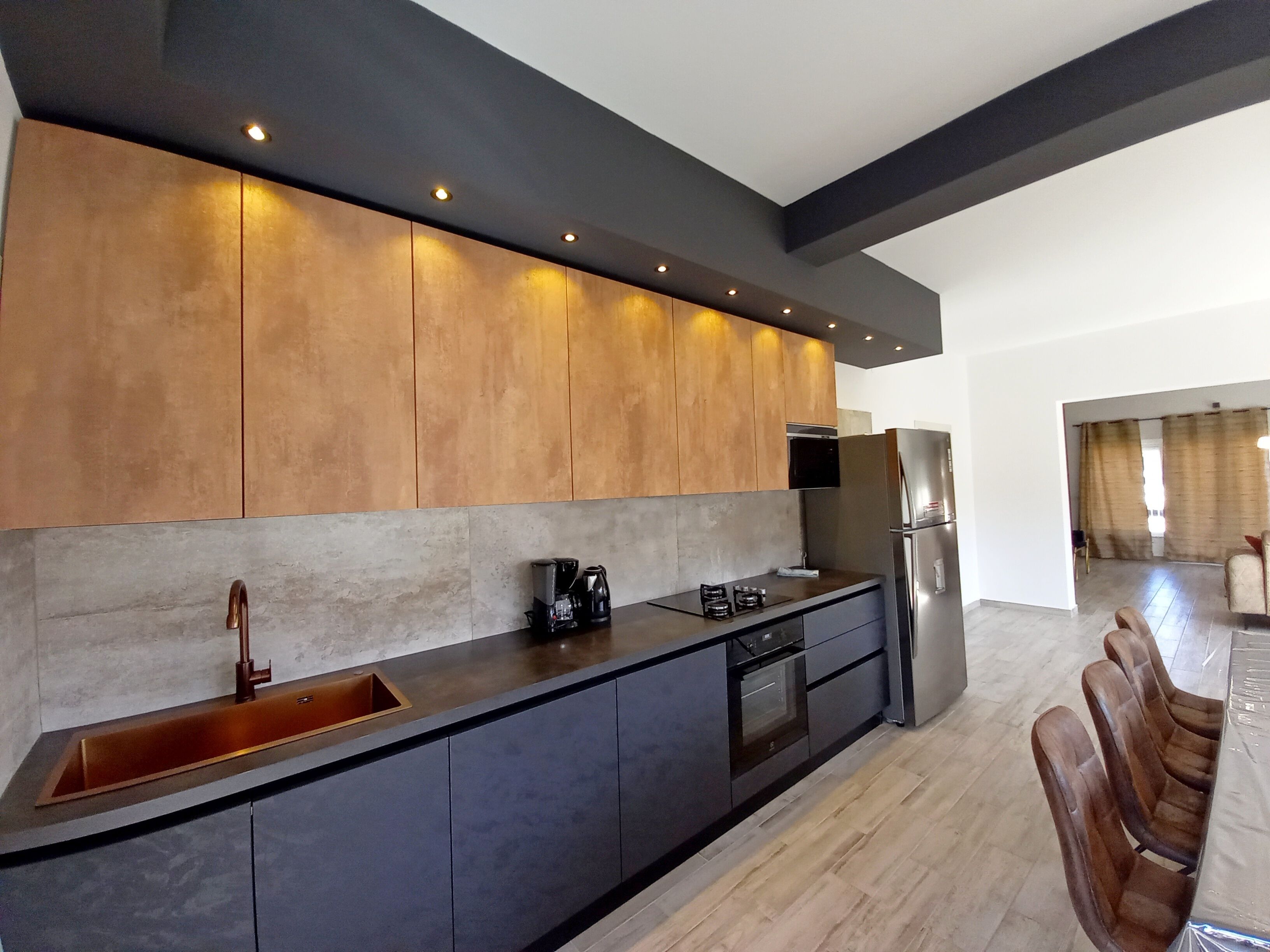 A modern kitchen with a built-in oven, a stainless steel refrigerator, and a dark countertop.