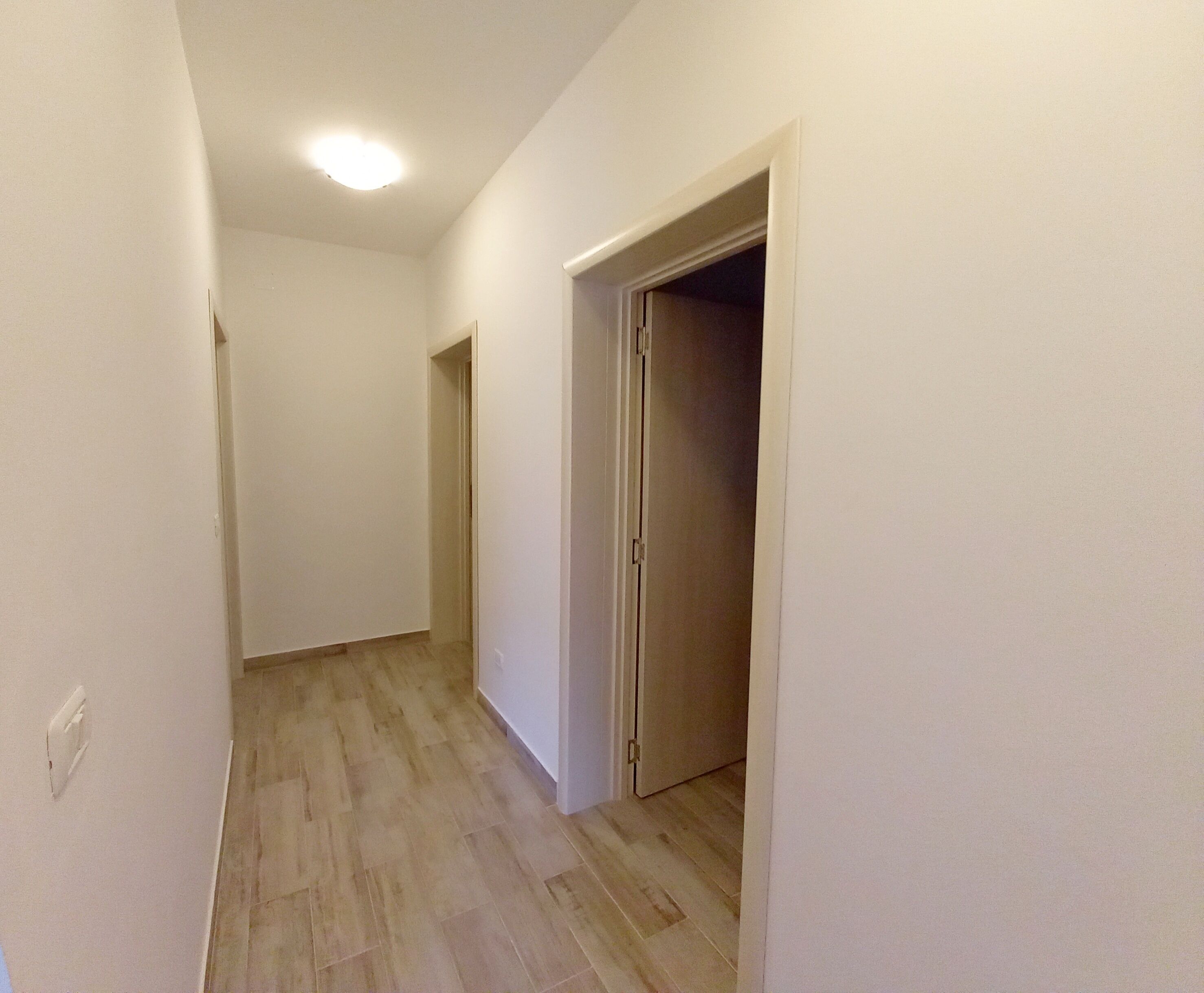 A narrow hallway with wooden flooring and white walls, leading to a closed door at the end.
