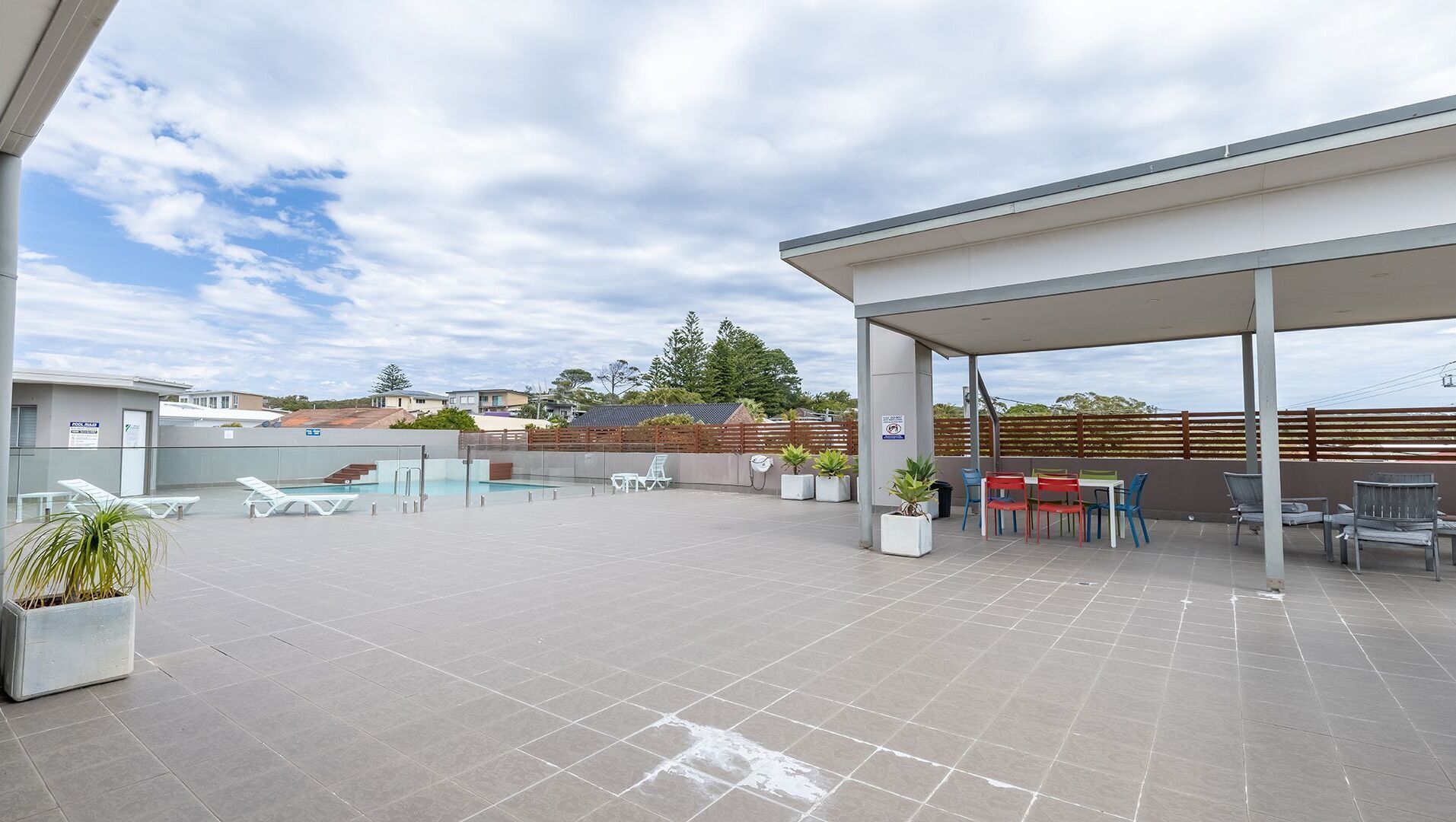 Un espacio al aire libre techado con piscina, sillas de descanso y una mesa con sillas.