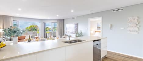 Een moderne keuken met een centraal eiland, een eethoek met uitzicht, en een woonruimte met een bank en planten.