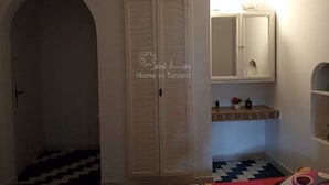 A room with a checkered floor, a white wardrobe, and a small shelf with decorative items.