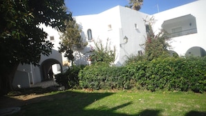 A white building with a small garden area, a paved pathway, and a visible archway.