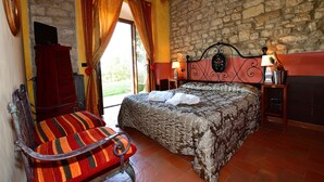 A bedroom with a stone wall, a bed with a headboard, a wooden chair, and a nightstand with a lamp. - COUNTRY RESORT THE ASH (Toscana)