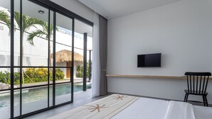 A modern hotel room with a large sliding glass door leading to a pool area, a bed with a starfish design, a television on the wall, and a small wooden shelf. - Villa Lapis by Villa Finder (Canggu)