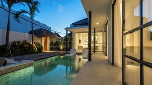 A modern pool area with a clear pool, lounge chairs, and a thatched-roof structure. - Villa Lapis by Villa Finder (Canggu)
