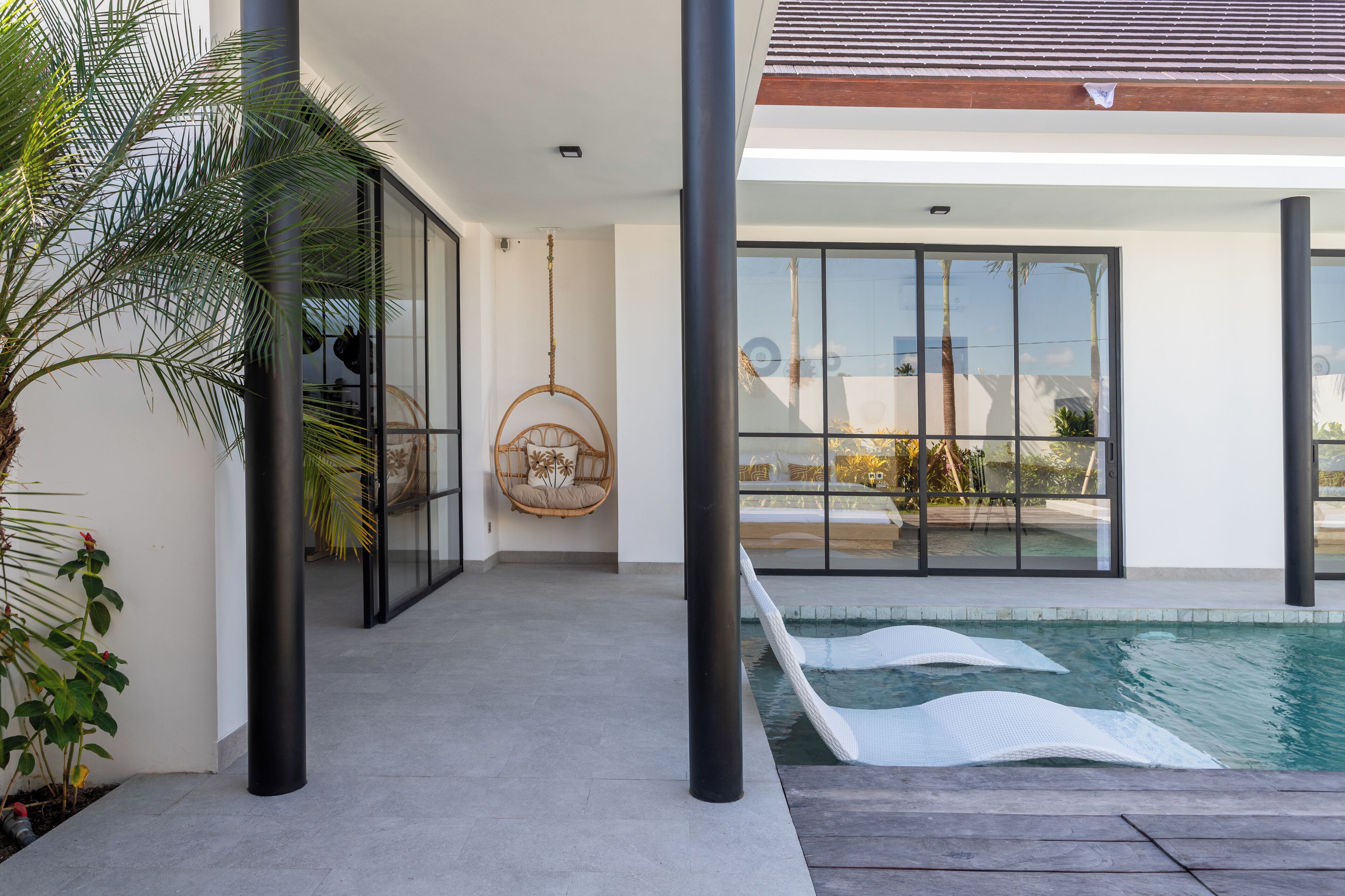 Una casa moderna con puerta de vidrio que da a una zona de piscina, una silla colgante y vistas del paisaje circundante.