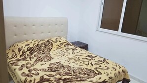 Ein Schlafzimmer mit einem Bett, das mit einer Bettdecke mit Tigerprint versehen ist, einem gepolsterten Kopfteil und einem Fenster mit Jalousien.