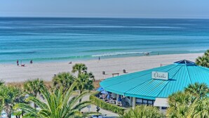 Vista de la playa con un edificio al primer plano, identificado con el letrero "Oceans", que presenta un techo azul y una señal.
