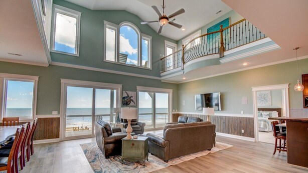 A spacious living area with a large window overlooking the ocean, a ceiling fan, and a dining area with a view. - Majestic View: Luxurious 8-bedroom oceanfront home in North Topsail Beach for up to 30 guests. (North Topsail Beach)