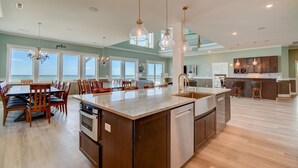 A spacious kitchen with a large island, wooden chairs, and pendant lighting. - Majestic View: Luxurious 8-bedroom oceanfront home in North Topsail Beach for up to 30 guests. (North Topsail Beach)