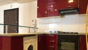 Une cuisine de taille réduite, équipée d’un lave-linge, d’une cuisinière et de meubles de rangement rouges.