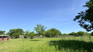 A grassy field with a wooden fence, a small building, and red chairs. - Sunrise Sunset Peaceful Country Cabin  (Bruceville)