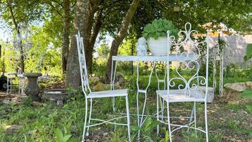 A garden area with a white metal table and chairs, surrounded by greenery and trees.