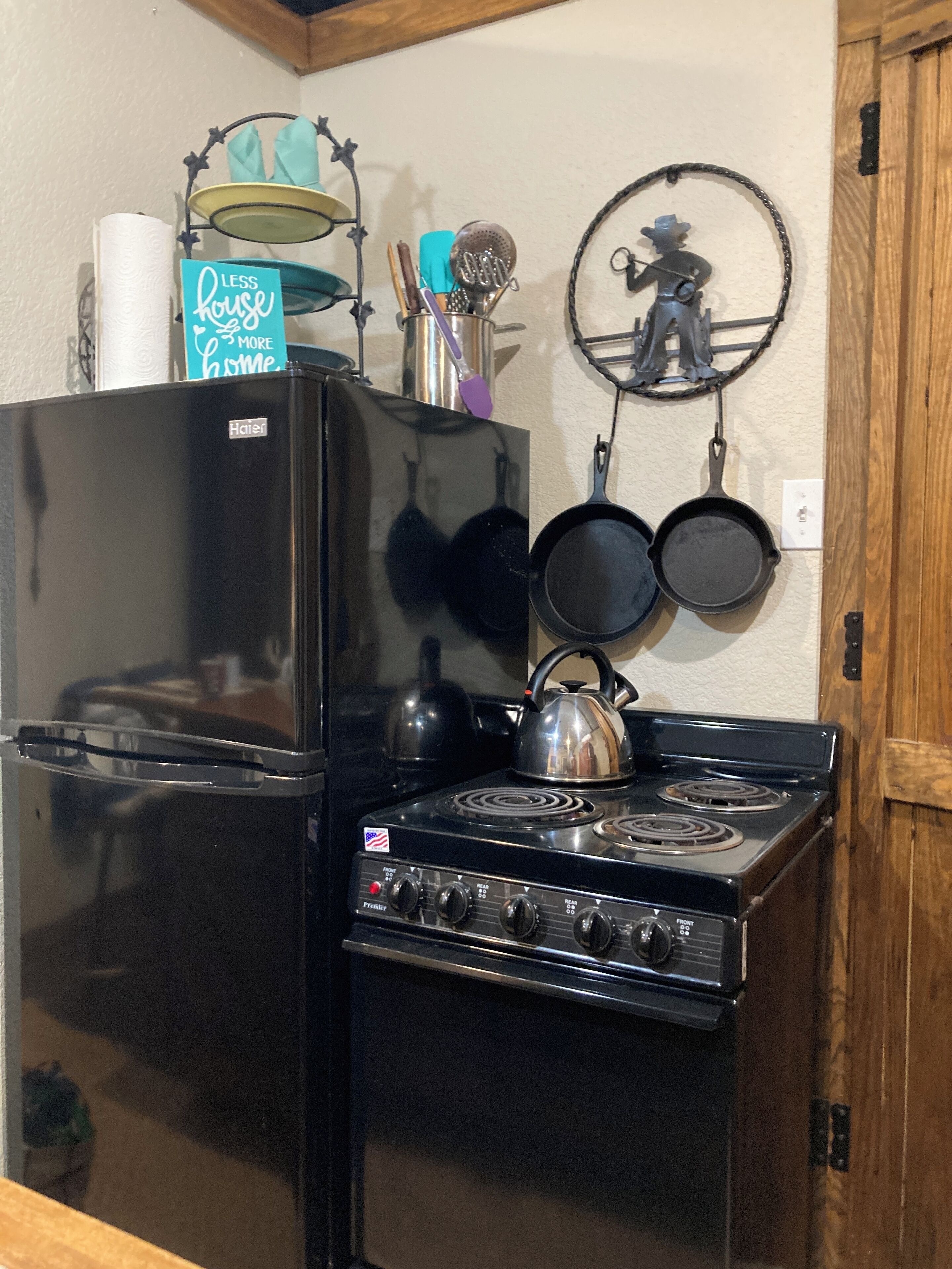 A kitchen with a black refrigerator, a stove, and a wall-mounted pot rack with pans.