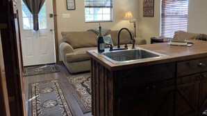 A compact living space with a kitchenette, a sofa, a dining table, and a window with blinds. - Sunrise Sunset Peaceful Country Cabin  (Bruceville)
