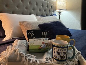 Un lit bien fait, avec une boîte de thé détox « SleepyTime », une tasse ornée d’une citation motivante et une lampe en arrière-plan.