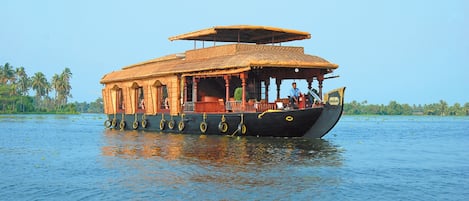 A traditional wooden houseboat with a thatched roof, multiple windows, and a black hull.