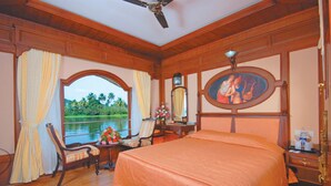 Une chambre avec un grand lit, un bureau avec une chaise, une vue sur un lac et un ventilateur de plafond.