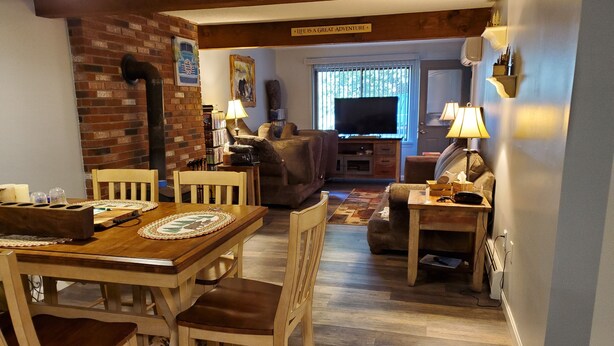 A cozy living room with a fireplace, a dining area with a wooden table and chairs, and a comfortable seating area with a couch and a TV. - Beautiful condo right near all North Conway, Jackson and Bartlett has to offer! (Bartlett)