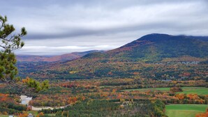 A panoramic view of a mountainous landscape with autumn foliage, a river, and scattered buildings. - Beautiful condo right near all North Conway, Jackson and Bartlett has to offer! (Bartlett)