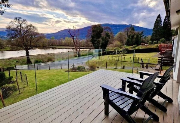 A deck with outdoor seating, a view of a lake, and mountains in the background.