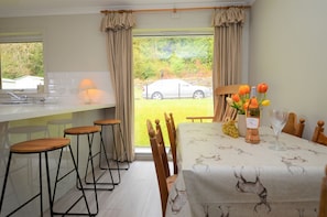 A dining area with a table set for four, a window with curtains, and a view of a car outside.