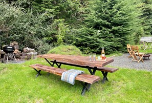 A wooden picnic table with benches, a grill, and outdoor seating. - Nursery Cottage - Benmore -  woodland setting, sleeps 4 guests (Benmore, Dunoon)