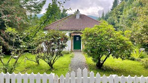 A quaint cottage with a green door, surrounded by lush greenery and a white picket fence. - Nursery Cottage - Benmore -  woodland setting, sleeps 4 guests (Benmore, Dunoon)