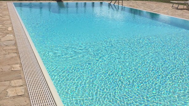 A rectangular swimming pool with clear blue water, surrounded by a stone deck.