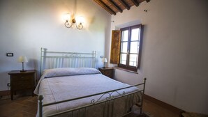 A bedroom with a metal bed frame, two bedside tables with lamps, a wooden window with shutters, and a wall-mounted light fixture.