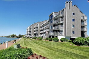 A multi-story residential building with balconies, a well-maintained lawn, and a waterfront view.