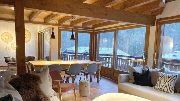 A cozy interior with a wooden dining table, chairs, a sofa, and a round wooden coffee table.