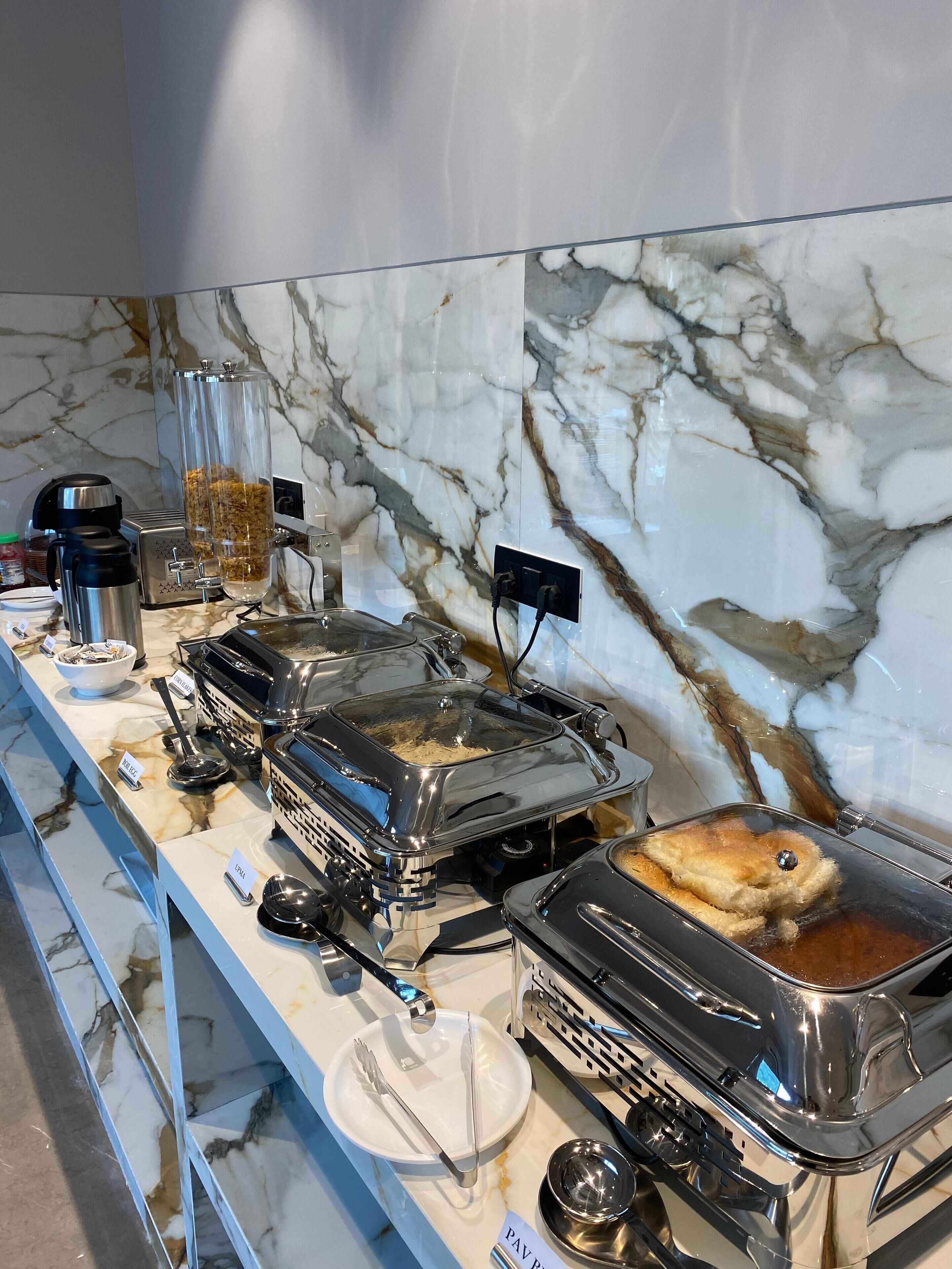 A buffet setup with various food stations, including a griddle and a hot dish, on a marble countertop.