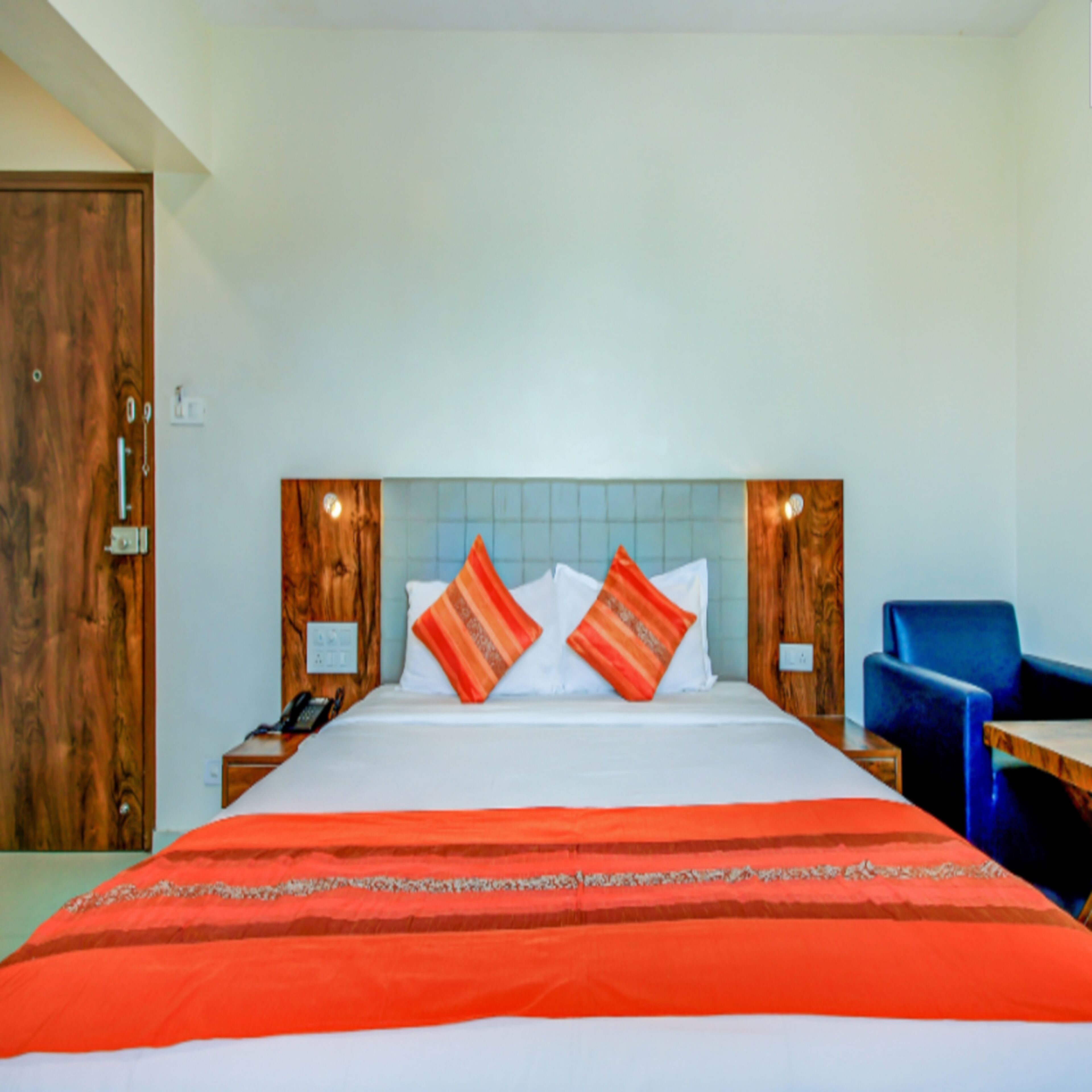 A hotel room with a bed, a nightstand, a chair, and a wooden door.