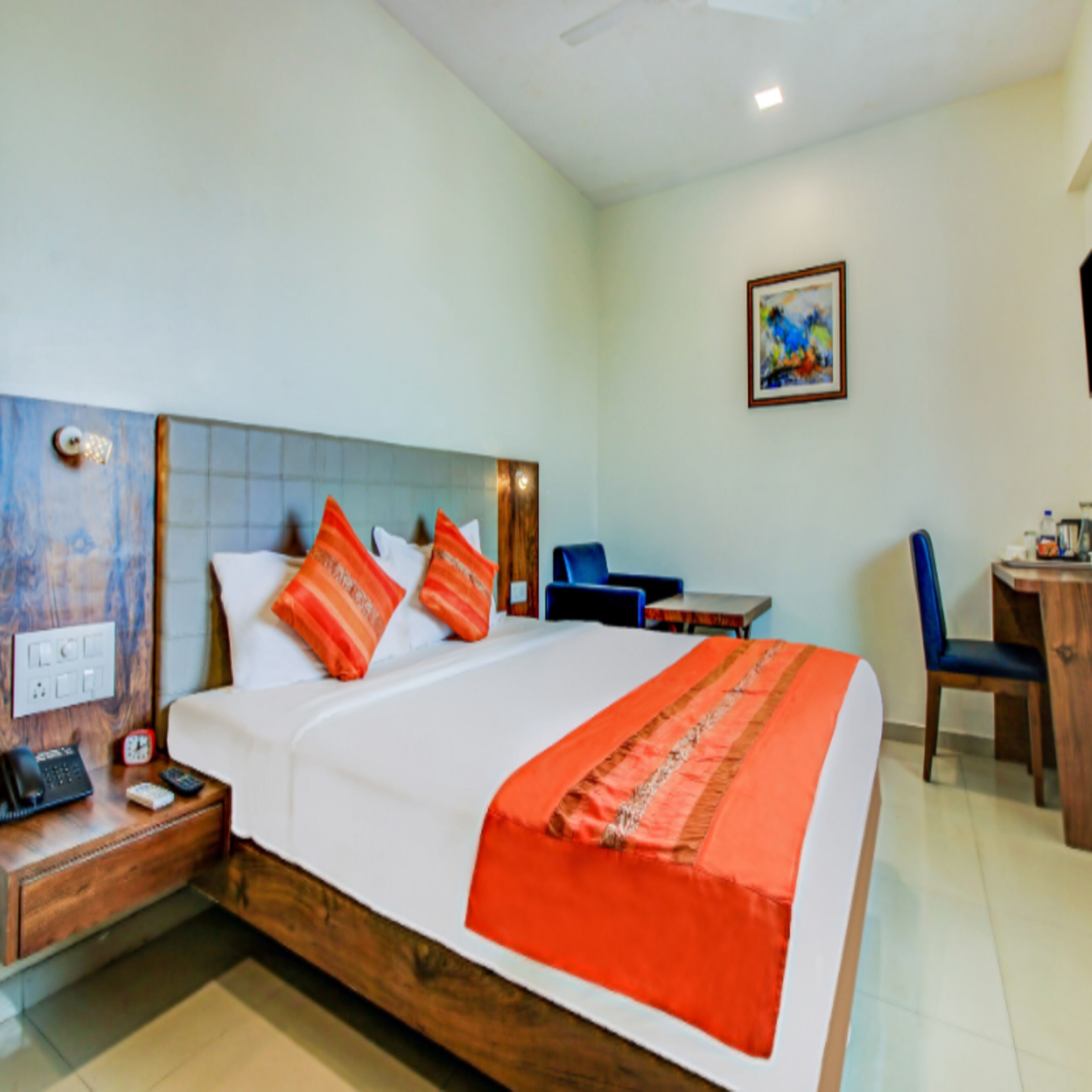 Quarto de hotel com cama, escrivaninha, cadeira, telefone e uma pintura na parede.