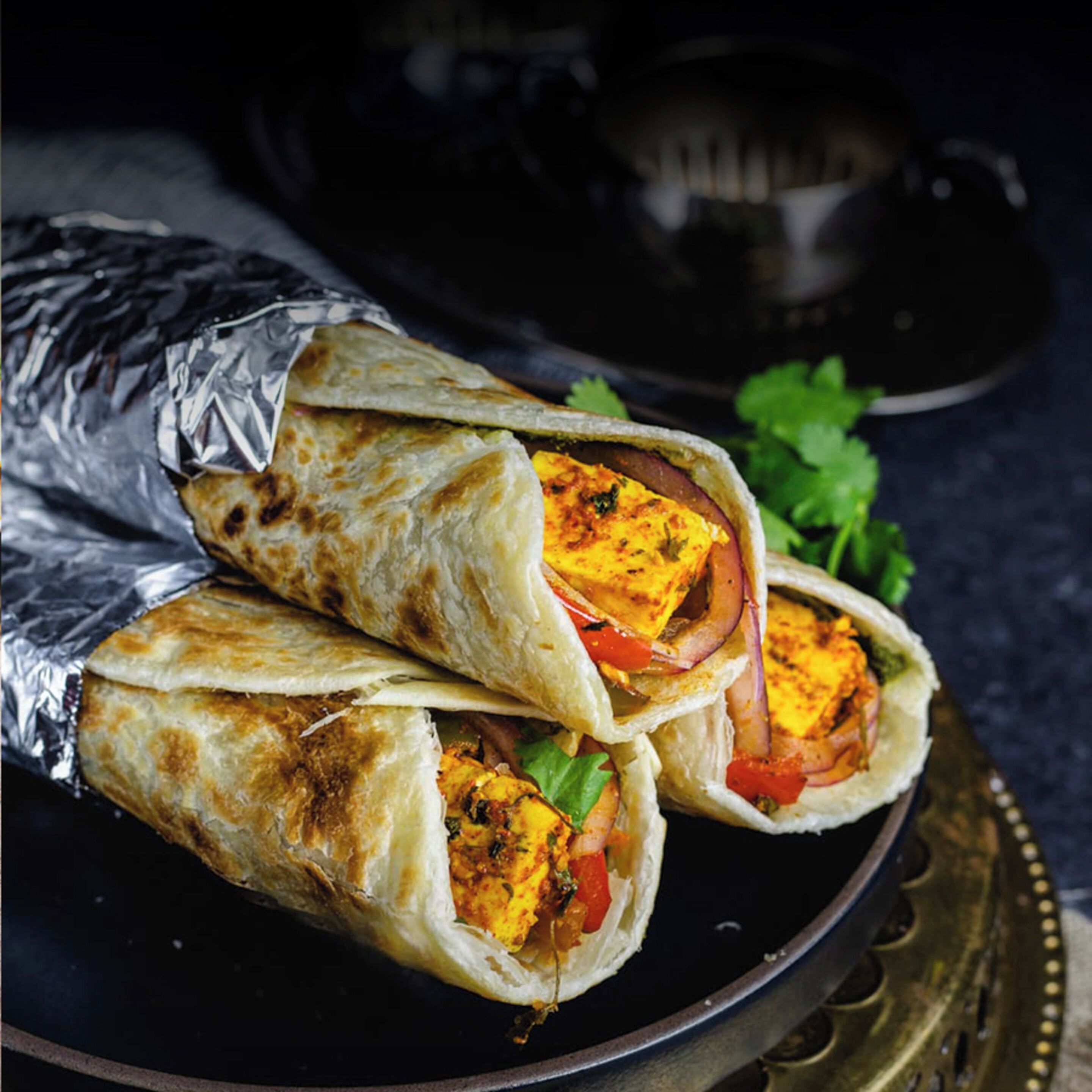 A plate with a wrap containing paneer and vegetables.