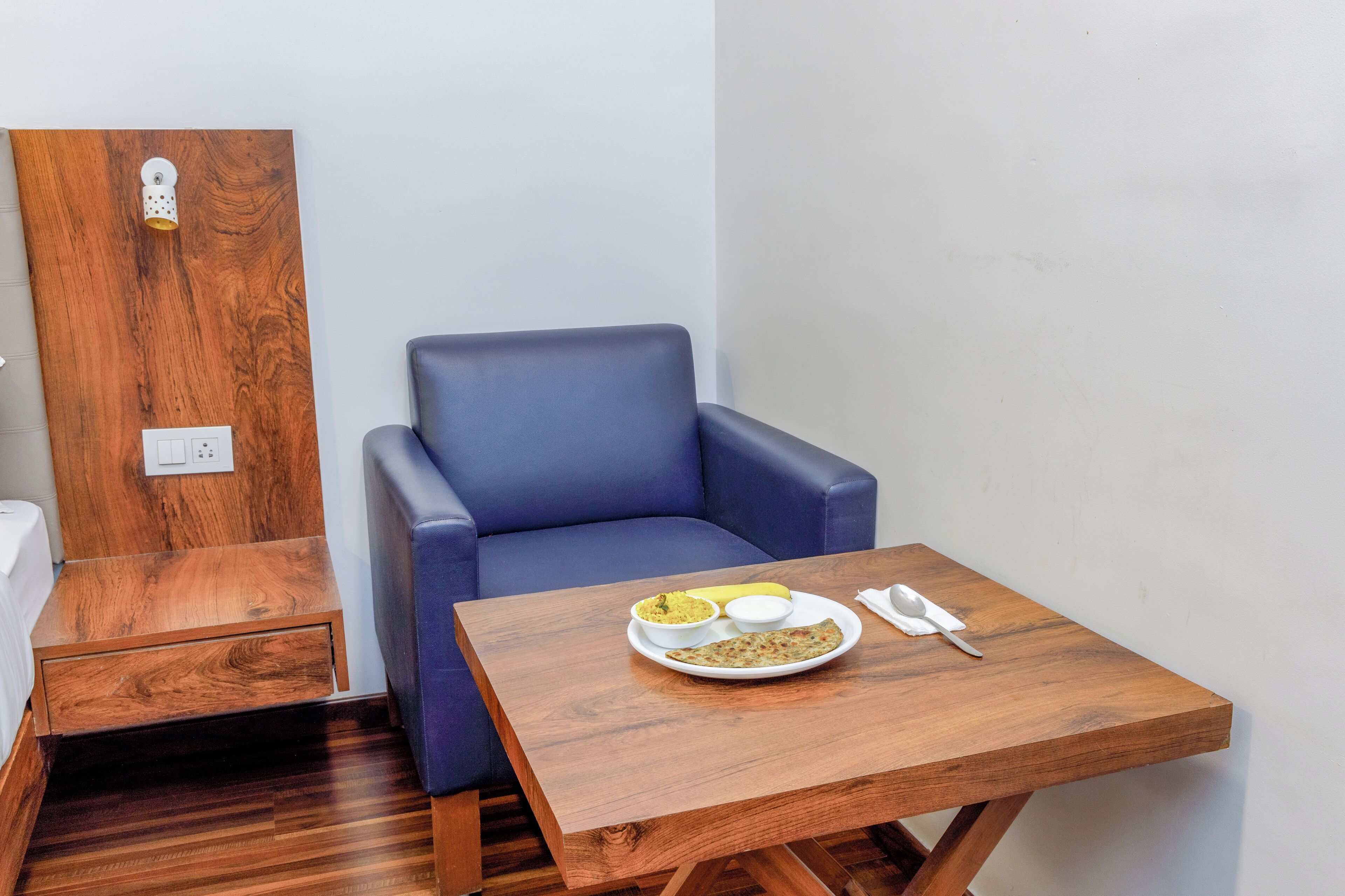 A small room with a wooden table, a blue chair, and a bed.