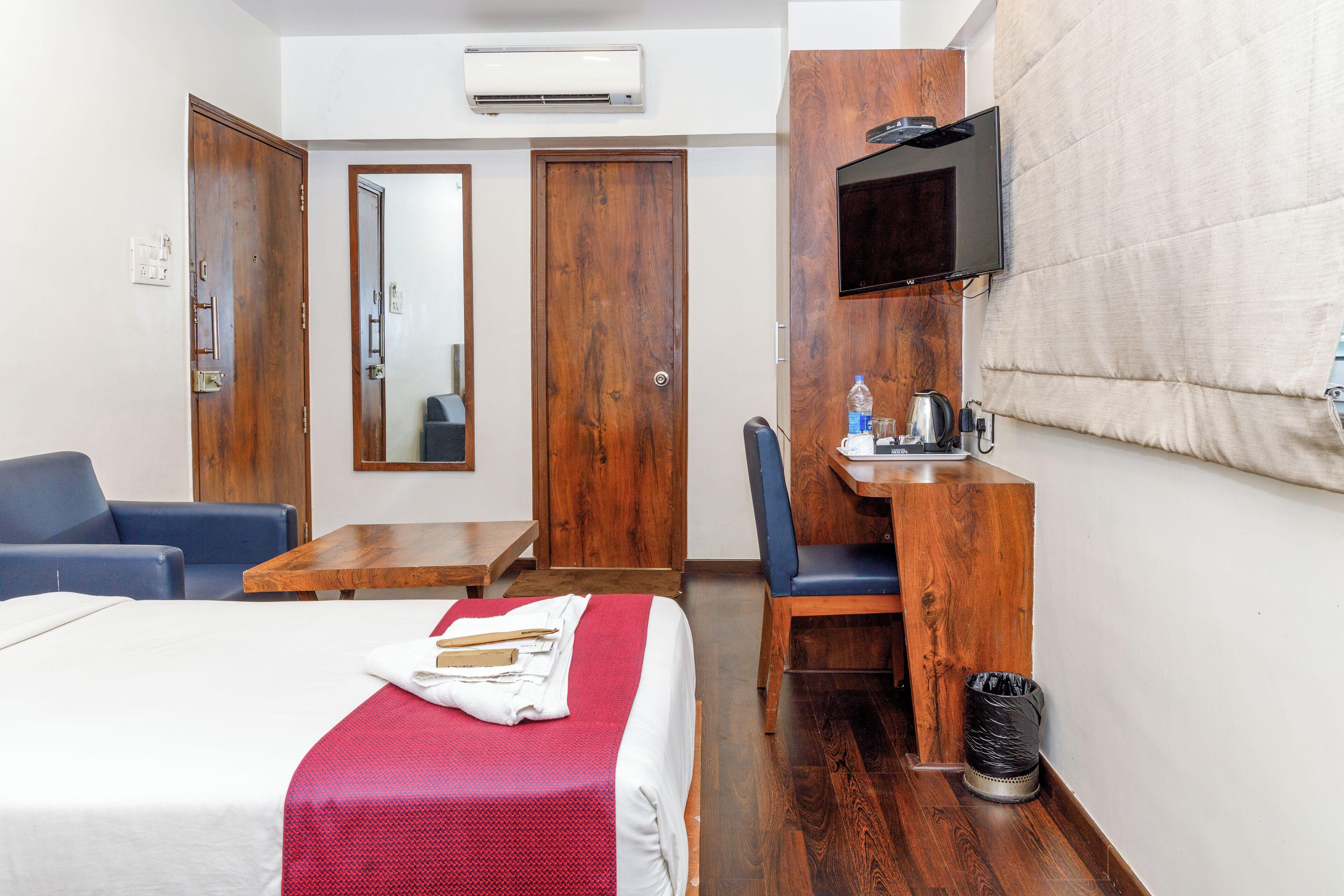 A hotel room with a bed, a desk, a chair, a TV, and a mirror.