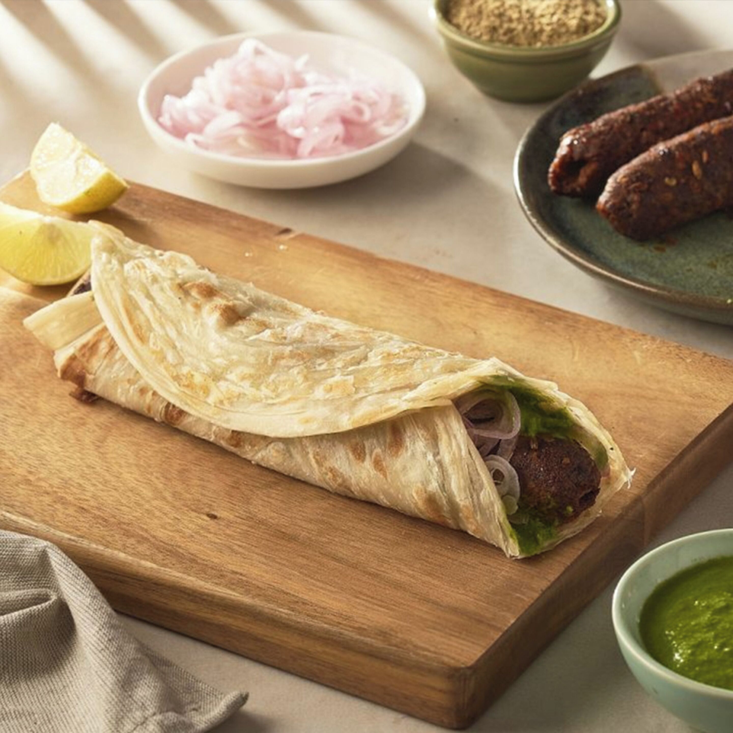 Wrap met vlees en groenten op een houten plank, vergezeld van partjes citroen, gesneden uien en een schaaltje groene saus.