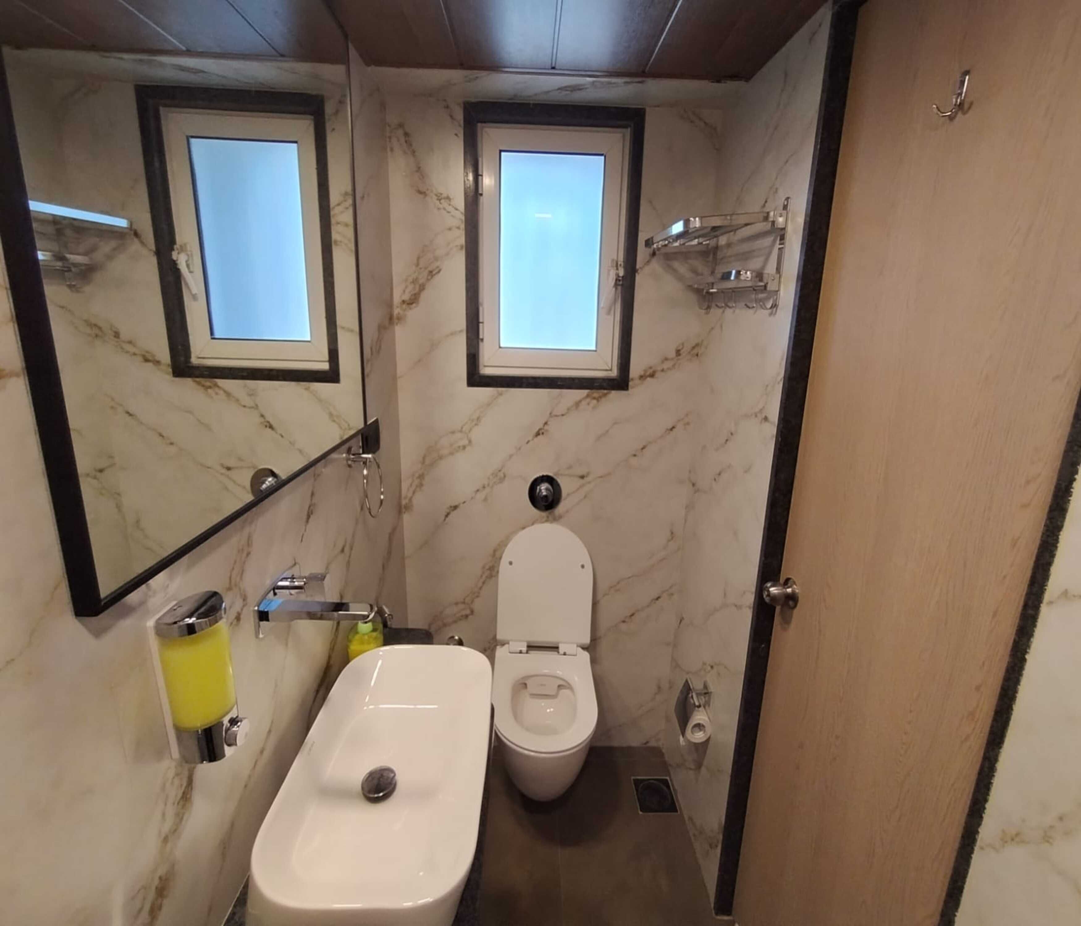 Een badkamer met een marmeren wand, toilet, bidet, wastafel en twee ramen.