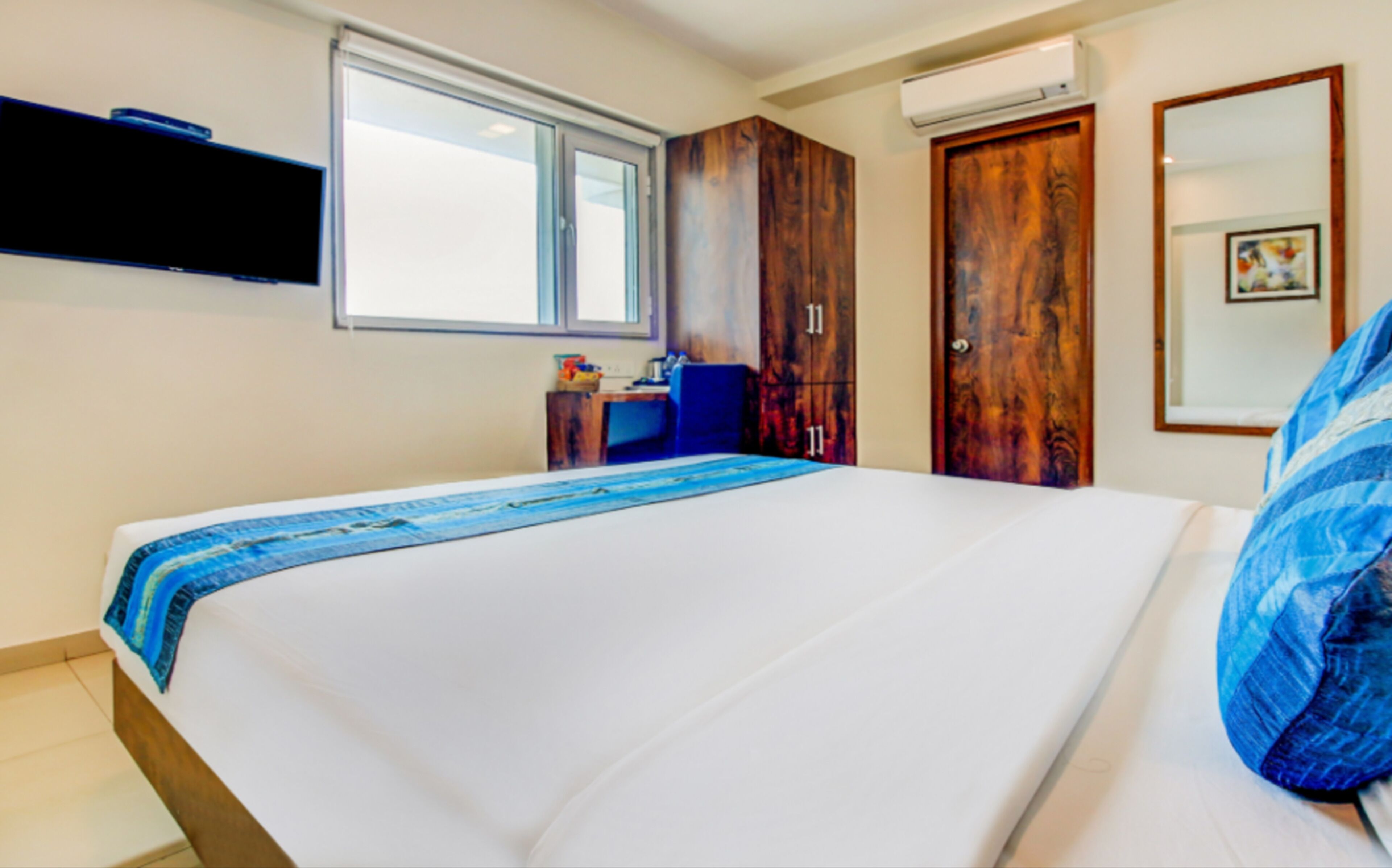 A bedroom with a large bed, a desk, a wardrobe, and an air conditioning unit.