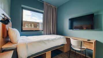 A modern hotel room with a bed, a desk, a chair, a TV, and a window with curtains.