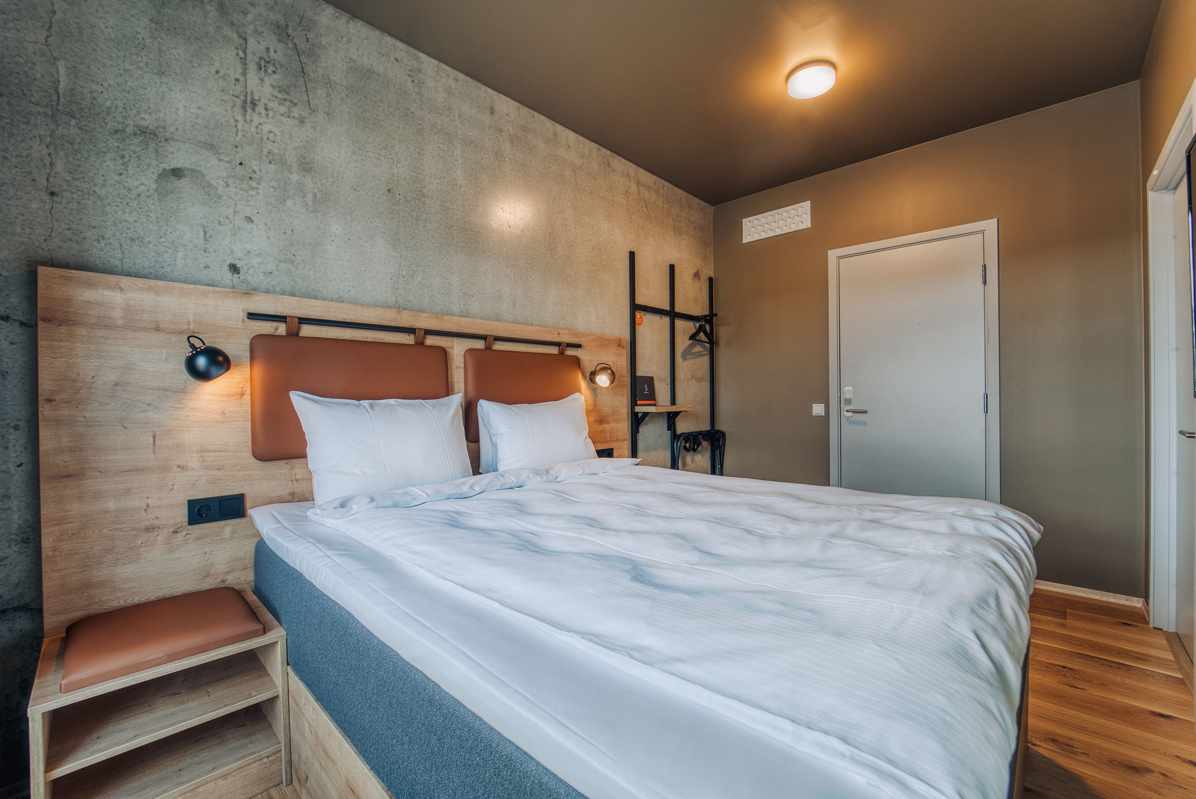 Una camera da letto con una testiera in legno, un letto con biancheria bianca, un comodino con una lampada e un armadio con specchio.