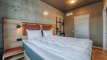 A bedroom with a wooden headboard, a bed with white bedding, a nightstand with a lamp, and a wardrobe with a mirror.