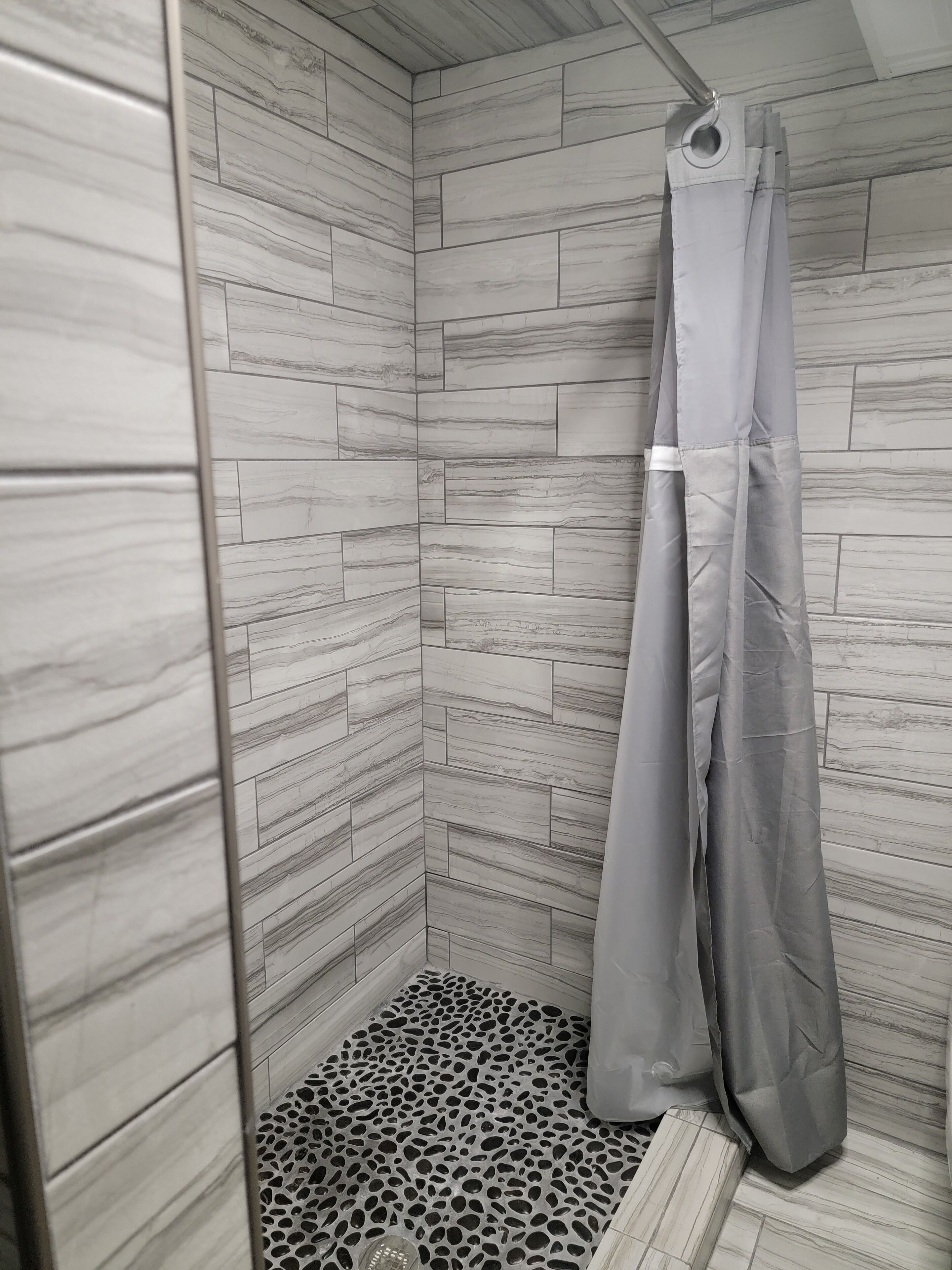 A shower with a grey curtain and a patterned floor.